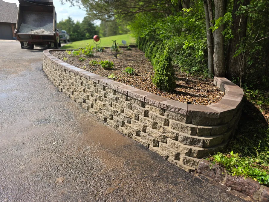 Curved retaining wall beside a driveway with mulch and planted beds
