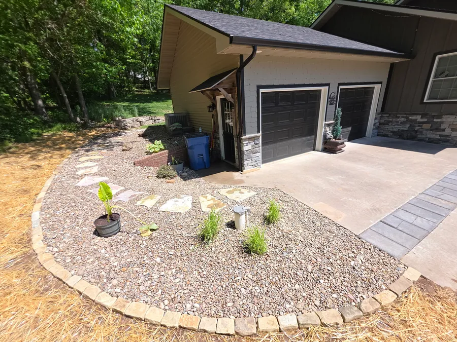Clean front bed with rock, plants, and paver walkway beside a garage